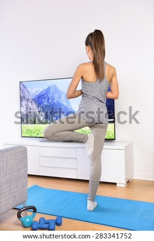 Yoga video class - woman training at home in living room in front of the television following a fitness program or watching her favorite TV show.