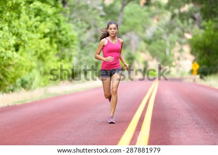 Running fit woman - female runner training outdoors jogging on red road in amazing landscape nature. Fit beautiful fitness model working out outside in summer.
