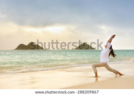Yoga woman meditating in warrior pose relaxing outside on beach at sunrise. Female yoga girl working out training in serene ocean landscape. Lanikai beach, Oahu, Hawaii, USA.