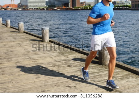 Low section of fit young man jogging on boardwalk. He is in sports clothing. Determined male jogger is exercising by river.