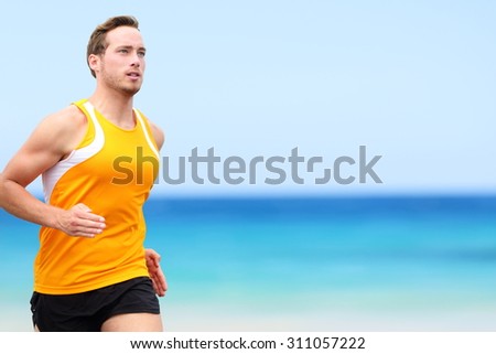 Handsome fit Running young man jogging on shore. He is in sports clothing. Determined male jogger is exercising at beach.