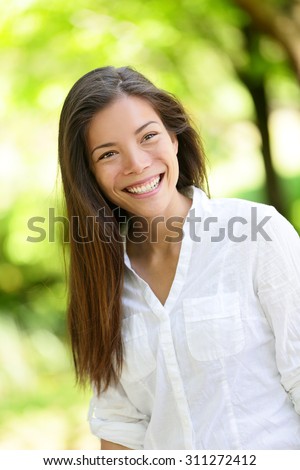 Beautiful happy young woman looking away. She is with long brown hair. Mixed race Asian / Caucasian female is in casuals at park.