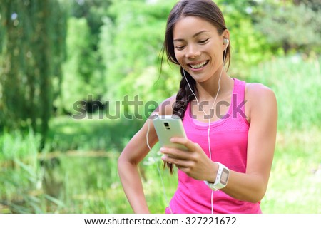 Woman runner sharing running data on social media after exercise. Girl listening to music on smart phone after jogging run in city park. Female jogger with earphones, smartphone and heart rate monitor