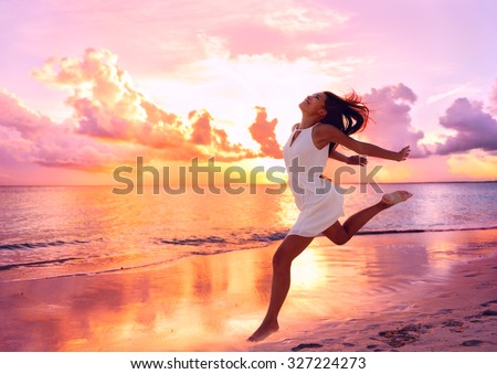 Happy beautiful free woman running on the beach at sunset jumping playful having fun in serene picturesque sunset at the ocean . Aspirational happy lifestyle with pretty young lady enjoying freedom.