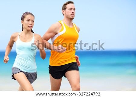 Runners running on beach. Jogging couple training on beach in full body length living healthy active lifestyle. Asian runner woman and fit male fitness athlete on run.