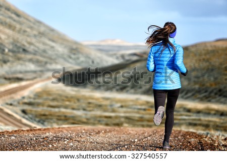 Woman winter and autumn running in down jacket. Female running jogging on mountain trail in beautiful landscape.