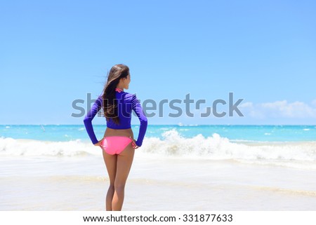 Beach woman in rash guard living an active lifestyle. Healthy young adult standing looking at waves before swimming wearing sun protective long sleeves swim shirt as solar protection against uv rays.
