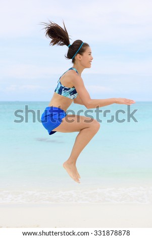 Crossfit fitness Asian woman on beach doing jump squat plyometric training exercises by jumping and touching knees as part of a full body core workout and active lifestyle.