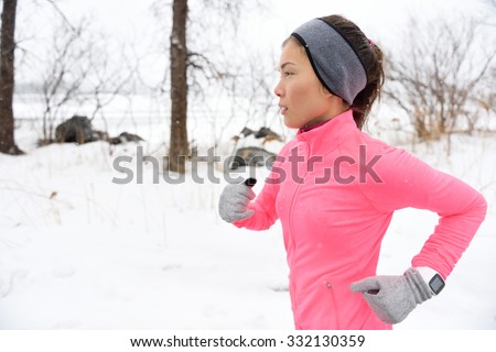 Female runner trail running in cold snowing weather. Asian Chinese athlete woman training for marathon jogging outside in snow wearing activewear jacket, headband, and winter gloves.