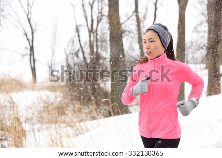 Winter jogging - young Asian Chinese adult woman runner running breathing cold air wearing pink windbreaker jacket, headband and gloves doing a cardio workout.