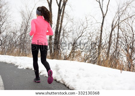 Winter jogging in park - female runner from the back exercising her cardio wearing pink jacket, active leggings and running shoes on city path.