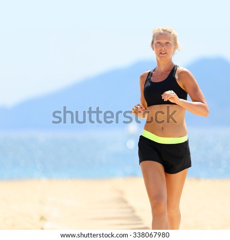 Young Caucasian woman in sportswear running at beach. Determined slim female is jogging on sunny day. She is representing healthy and fit lifestyle.
