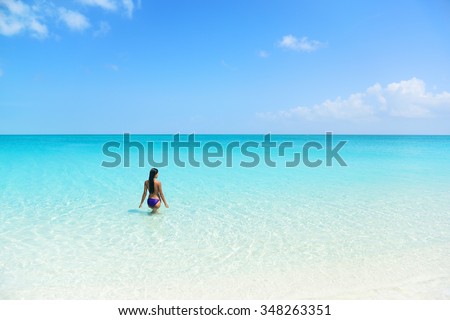 Beach holiday person swimming in blue ocean. Sexy bikini woman relaxing enjoying her tropical vacation in the Caribbean in a paradise destination with perfect turquoise water and white sand.