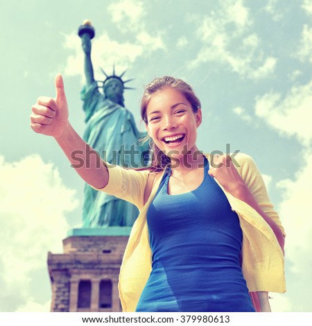Happy Asian Chinese tourist doing thumbs up having fun visiting the Statue of Liberty, american landmark in New York City. Famous touristic attraction, USA.