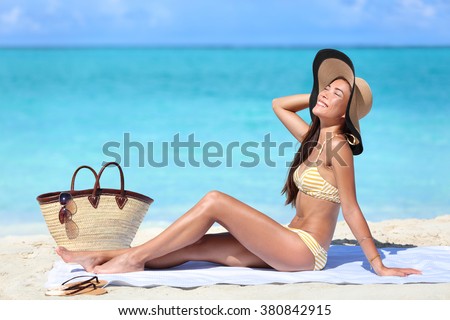 Beach woman sun tanning on summer tropical vacation wearing a cute retro stripes bikini and hat outfit with straw bag and towel.