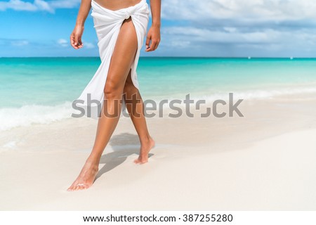 Caribbean vacation travel - woman leg closeup walking on white sand relaxing in beach cover-up pareo beachwear. Sexy lean and tanned legs. Sunmmer holidays, weight loss or epilation concept.