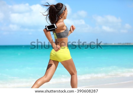 Fit woman cardio training doing running workout on beach. Unrecognizable athlete runner jogging fast on summer ocean background wearing a phone armband holder for music listening on smartphone app.