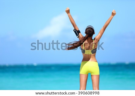 Strong fitness athlete arms up in success on summer beach after cardio training workout. Female runner woman running winning reaching goal achievement during strength training showing power.