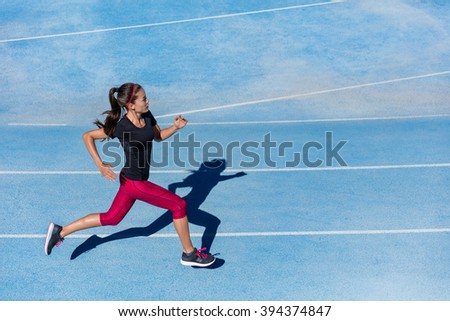 Athlete runner running on athletic track training her cardio. Jogger woman jogging at fast pace for competition race on blue lane at summer outdoor stadium wearing red capri tights and sports shoes.