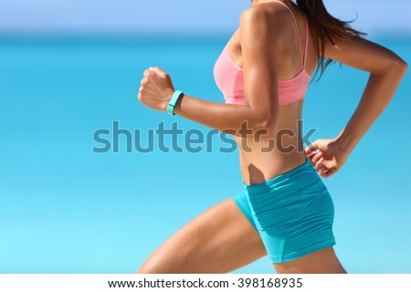 Wearable tech smart watch closeup, active woman wearing activity tracker bracelet on wrist. Runner girl running fast intense run outdoor on beach ocean background living a healthy life. Legs closeup.