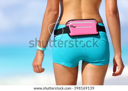 Running sports gear wearable tech female runner wearing fitness smart watch and smartphone holder waist pack for listening to music during outdoor workout. Closeup of shorts and behind.