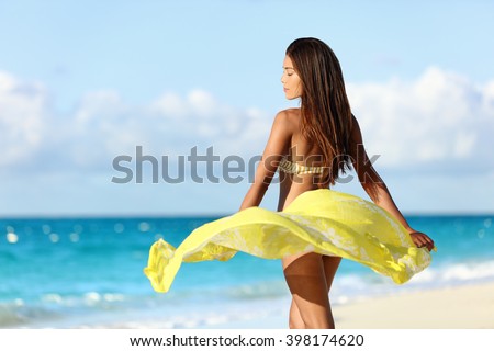 Carefree beautiful sexy bikini body woman relaxing in yellow flowing cover-up beachwear fashion wrap on ocean sunset background. Weight loss thighs cellulite and skincare spa beauty care concept.