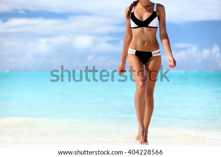 Sexy bikini body woman sun tanning relaxing on perfect tropical beach and turquoise ocean water. Unrecognizable model walking in fashion swimwear with smooth tanned skin and long lean legs.