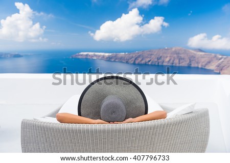 Travel vacation woman relaxing enjoying Santorini looking at famous view of Caldera. Young lady lying down on sun bed sofa lounge chair on holidays. Amazing view of sea. Europe travel destination.
