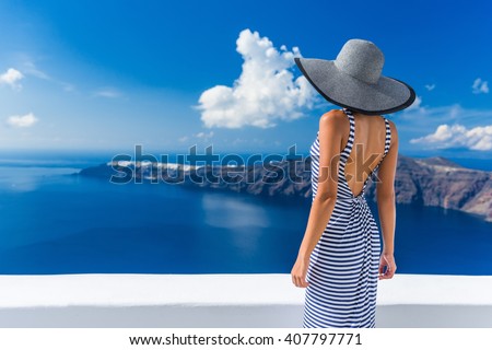 Luxury travel vacation woman looking at view on Santorini famous Europe travel destination. Elegant young lady living fancy jetset lifestyle wearing dress on holidays. Amazing view of sea and Caldera.