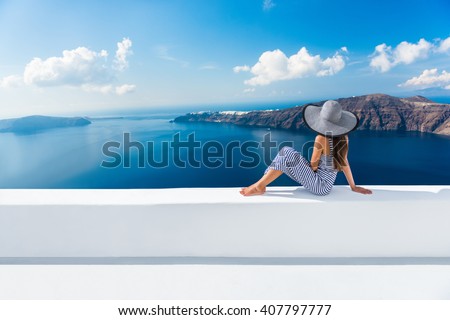 Europe Greece Santorini travel vacation. Woman looking at view on famous travel destination. Elegant young lady living fancy jetset lifestyle wearing dress on holidays. Amazing view of sea and Caldera