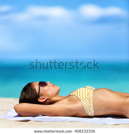 Beach vacation woman in bikini wearing sunglasses. Young lady sunbathing relaxing. Sexy young adult wearing eyewear for sun protection lying down on towel on sand tanning. Skincare UV sun care.