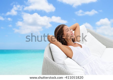 Sleeping woman relaxing lounging on white outdoor sofa day bed lounger on beach ocean background. Asian girl lying down laid back on pillows dreaming or enjoying the sun carefree happy. Home living.
