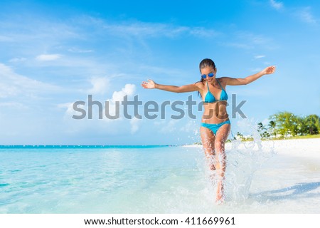Freedom carefree girl playing splashing water having fun on tropical beach vacation getaway travel holiday destination. Playful woman with abs slim bikini body relaxing feeling free.