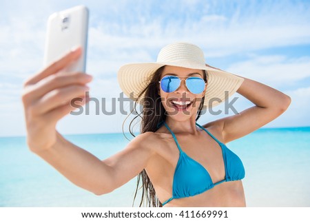 Selfie smartphone girl taking mobile phone photo on beach vacation during summer travel holidays. Sexy young bikini woman wearing fashion mirrored aviator sunglasses posing for camera having fun.