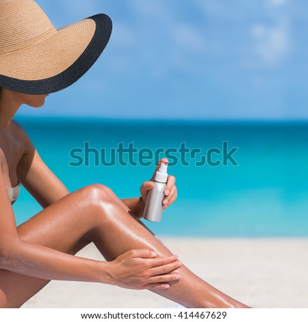 Beach body suntan skin care travel vacation. Bikini hat woman applying sunscreen lotion putting cream on tanned sexy legs sunbathing sun tanning sitting on sand with turquoise blue ocean background.