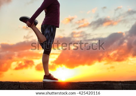 Running runner woman stretching leg muscle preparing for sunset trail run in outdoor summer nature. Female athlete lower body crop of feet doing legs stretches getting ready for cardio warmup.