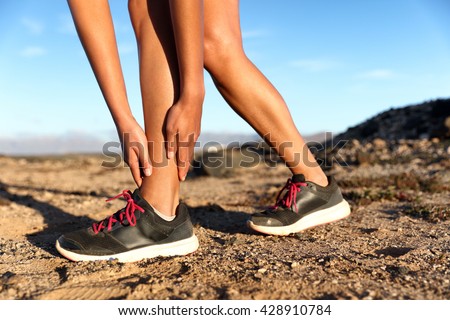 Runner woman with hurt ankles in pain during marathon. Athlete woman running outside with body injury. Sprained ankle on trail run in summer outdoors nature. Fitness leg accident on cardio workout.