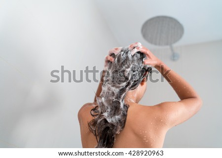 Shower woman washing hair showering in bathroom at home. Unrecognizable person from behind rinsing shampoo and conditioner from her long hair in warm bath with modern ceiling rain water nozzle head.