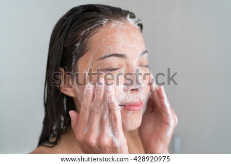 Skincare woman washing face in shower foaming facewash soap scrub on skin. Asian female adult cleaning body showering in hot water at home on in hotel as morning routine. Enjoying relaxing time.