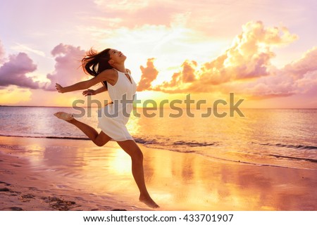 Freedom wellness well-being happiness concept. Happy carefree Asian woman feeling blissful jumping of joy on peaceful beach at sunset. Serenity, relaxation, mindfulness, stress free concepts.