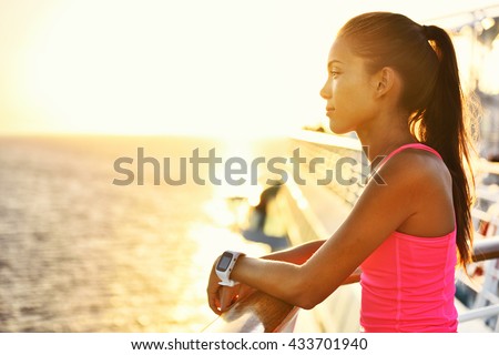 Active woman relaxing after run on cruise ship looking at the sea during summer holidays. Asian runner girl wearing smartwatch heart rate activity monitor living a healthy lifestyle.