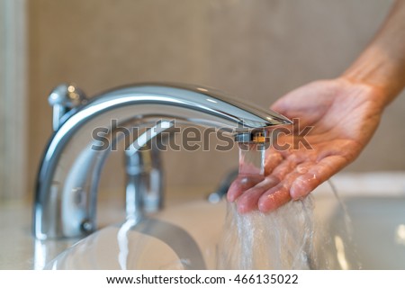 Woman taking a bath at home checking temperature touching running water with hand. Closeup on fingers under hot water out of a faucet of a sink or bathtub in house bathroom