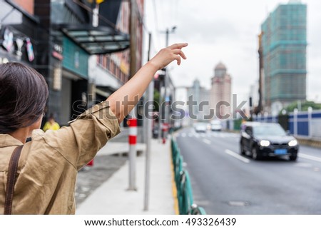 Hailing a rideshare black car on the road. Asian woman with hand up calling a taxi cab on Shanghai street, China using phone app technology for passenger to request a ride online.
