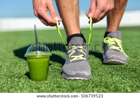 Green smoothie fitness man lacing running shoes, Athlete runner with green vegetable detox juice getting ready for morning run tying running shoe laces on grass. Fitness and healthy lifestyle concept.