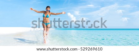 Sexy bikini body woman playful on paradise tropical beach having fun playing splashing water in freedom with open arms. Beautiful fit body girl on travel vacation. Banner crop for copy space.
