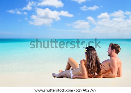 Happy couple relaxing sun tanning on vacation beach lying down on white sand looking at ocean copyspace background. Sunbathing on holiday.