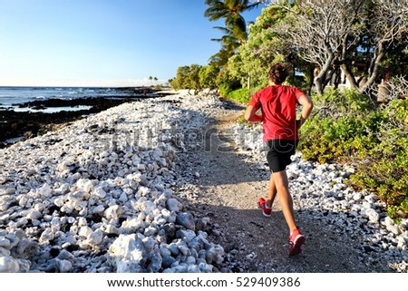 Trail runner jogging on running path at beach in white coral rocks at hawaii travel destination. Male athlete from behind doing cardio exercise outdoors in nature.