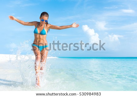 Sexy bikini body woman playful on paradise tropical beach having fun playing splashing water in freedom with open arms. Beautiful fit body girl on luxury travel vacation.
