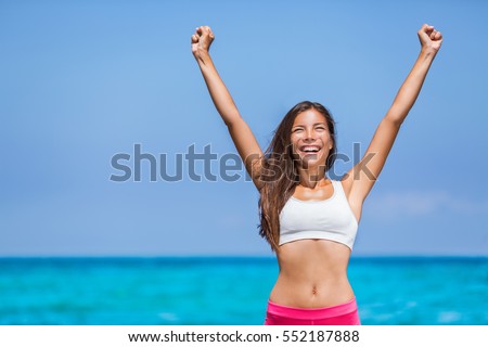Happy fitness success woman winner. Asian girl cheering arms up of joy on summer beach.