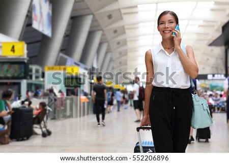 Businesswoman on commute transit talking on the smartphone while walking with hand luggage in train station or airpot going to boarding gate. Asian woman happy using mobile phone app for conversation.